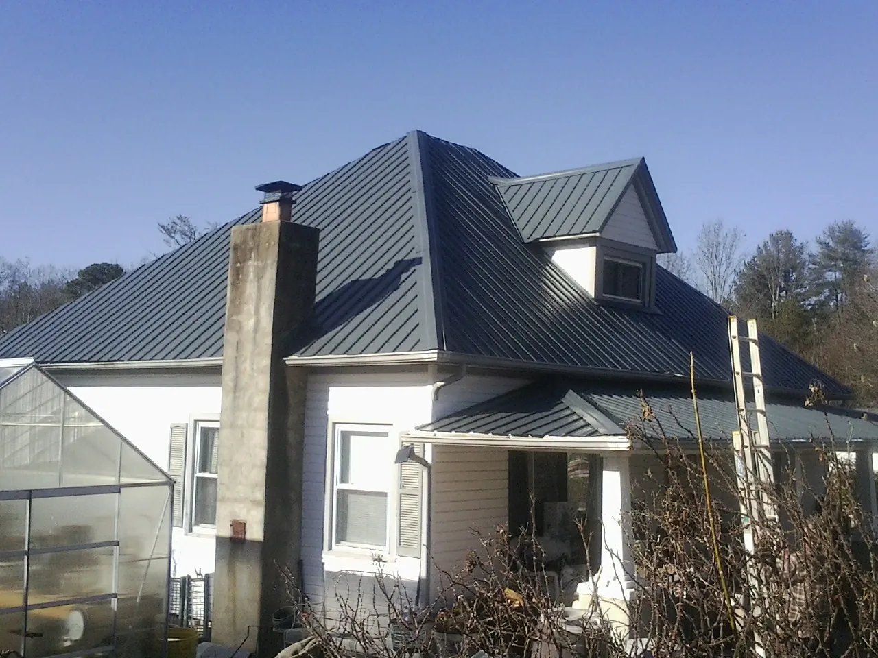 Dark blue standing seam metal roof on a white farmhouse with dormer — Slate & Tile Roof Repair by Roofing Brothers in Becker