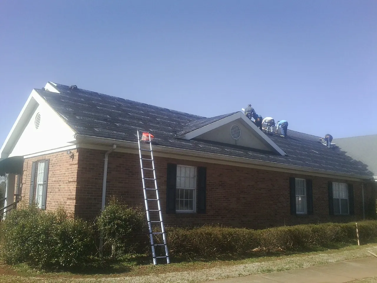 Crew tearing shingles off a brick ranch roof with a ladder set — Metal Roof Repair work by our crew in Becker