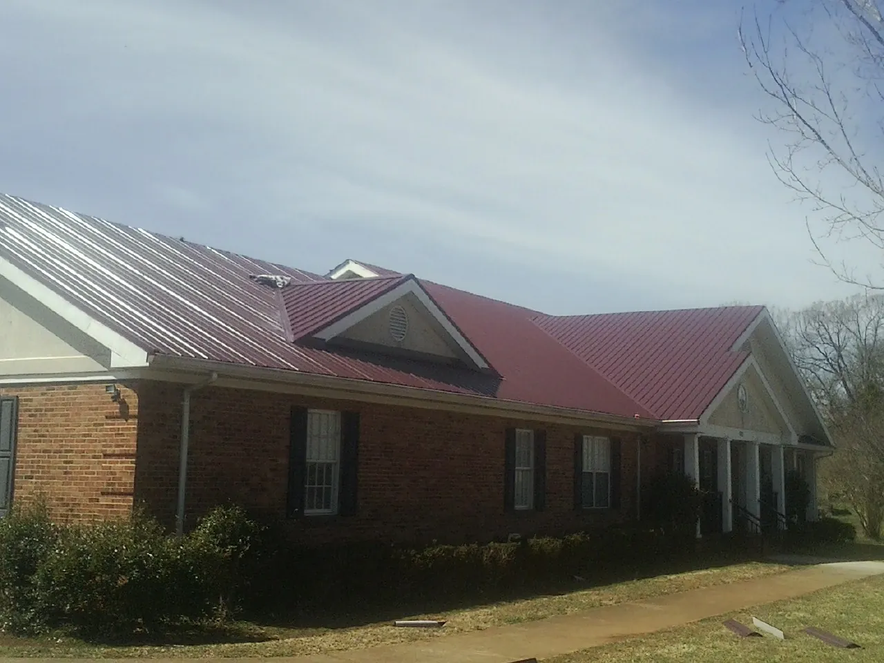 Red metal roof with gabled entries on a long brick building, from a Hail Damage Roof Repair job in Becker