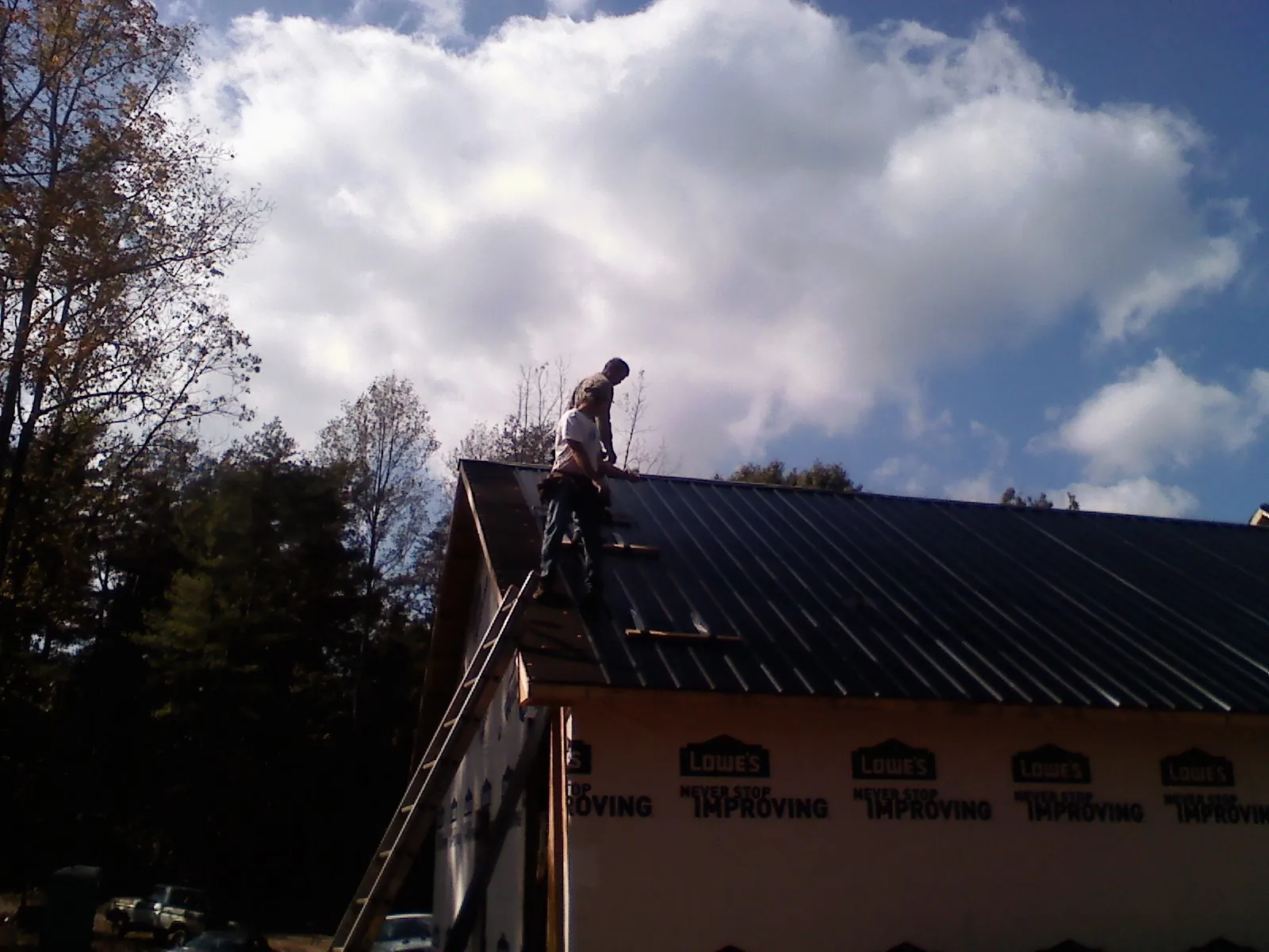 Roofer fastening dark metal panels high against a cloudy sky, from a Roof Inspection job in Becker