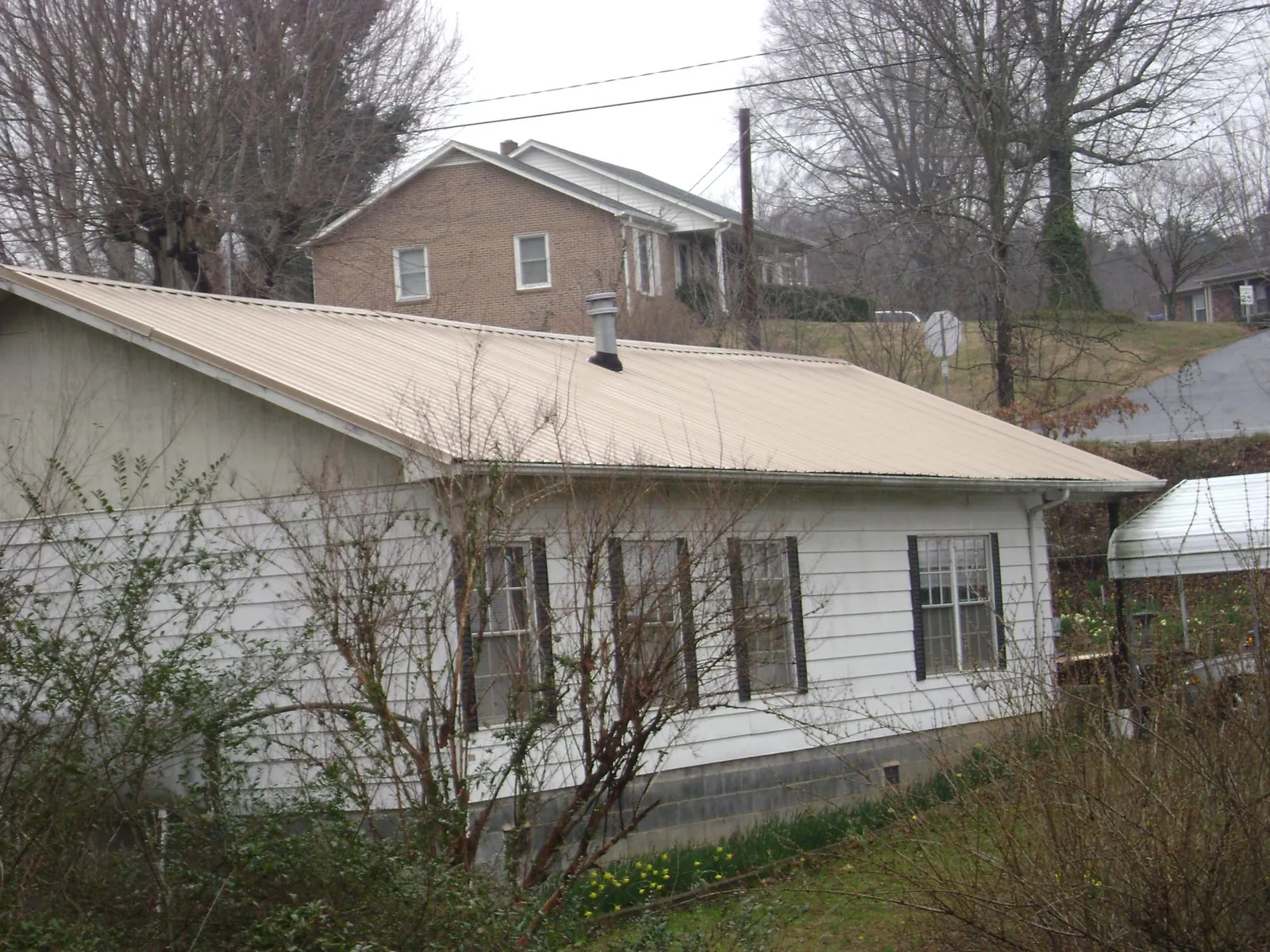 Tan metal roof on a white sided house set into a hillside — Commercial Roofing by Roofing Brothers in Becker