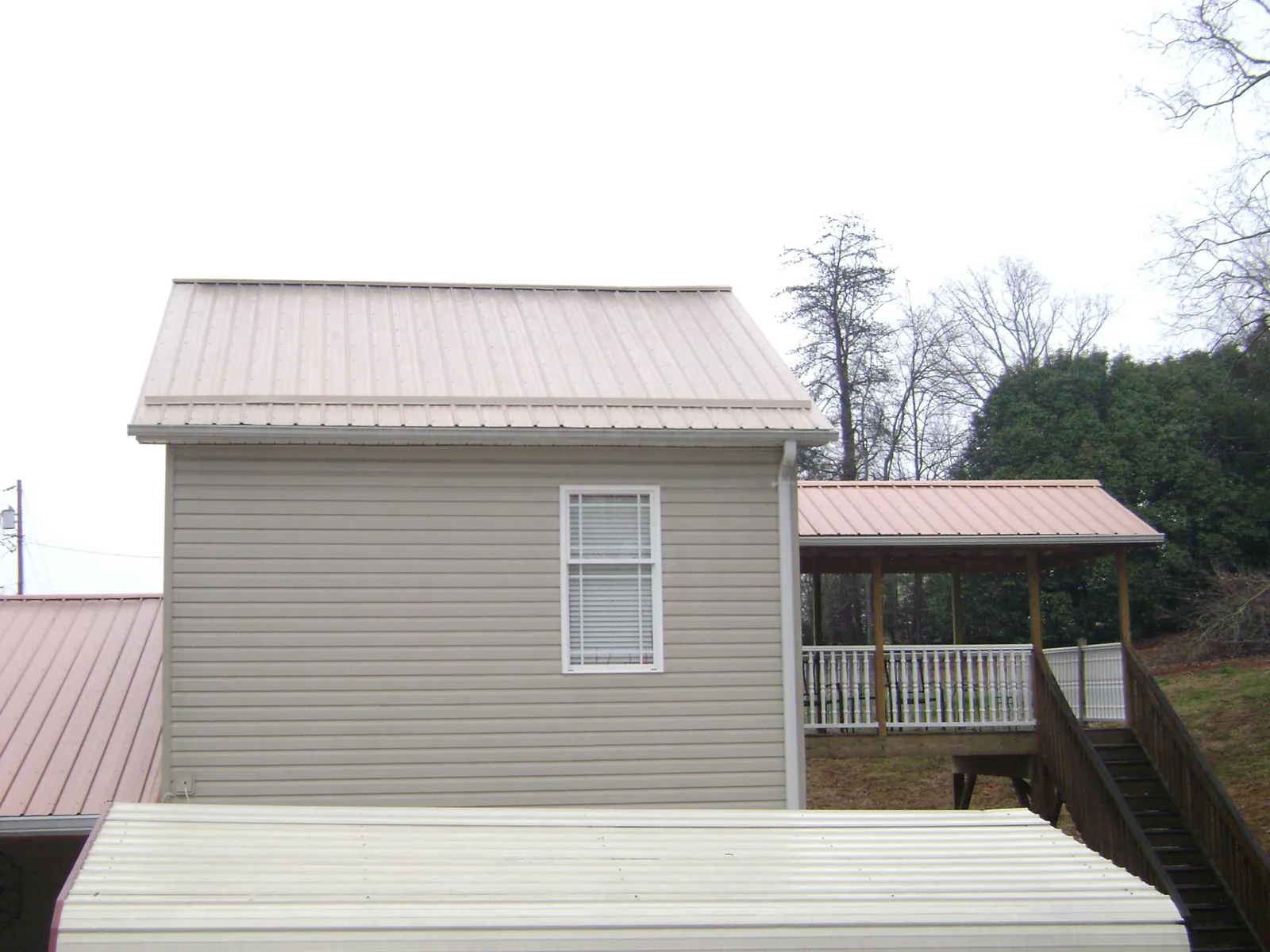 Tan metal roofs on a two story addition and attached porch, from a Roof Replacement job in Becker